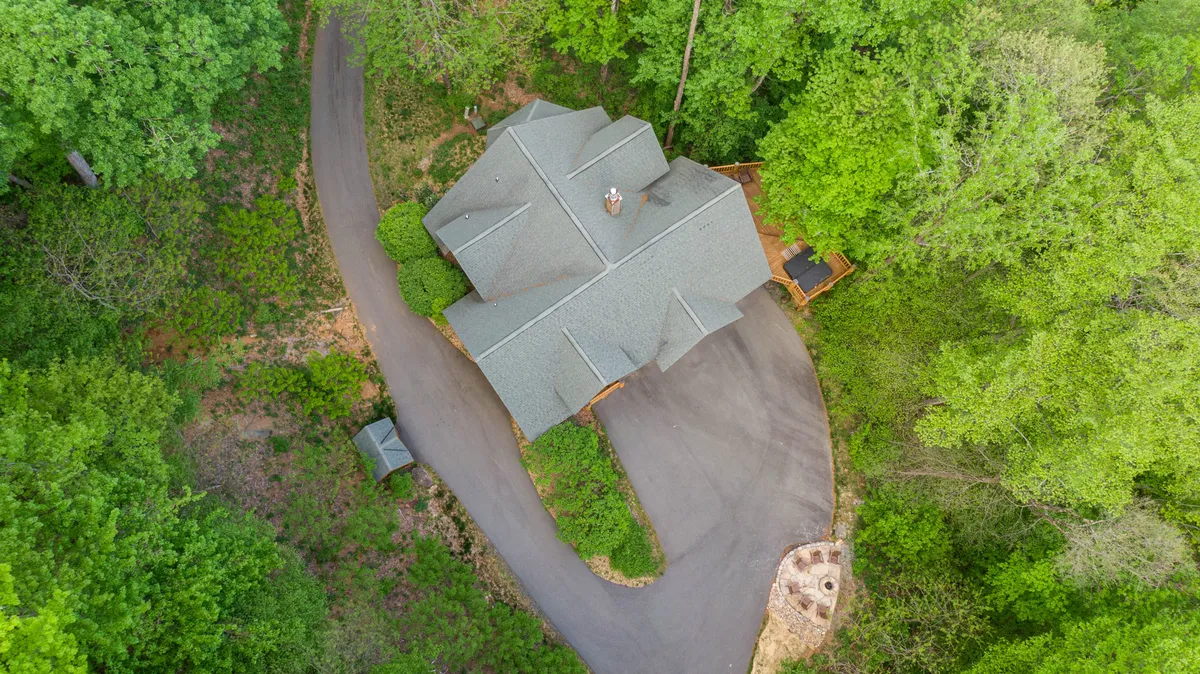 This image features the exterior of Buffalo Creek Lodge, nestled among mature trees with a curved driveway leading up to the house. The spacious surroundings and natural setting are clearly visible, suggesting abundant outdoor space that pets and their owners can explore together.