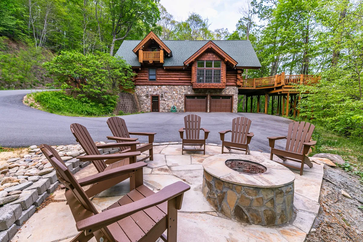 A welcoming log cabin exterior with a spacious deck, a fire pit surrounded by Adirondack chairs, and lush greenery. The setting is perfect for communal gatherings, enjoying sunsets, and relaxing in the crisp mountain air.