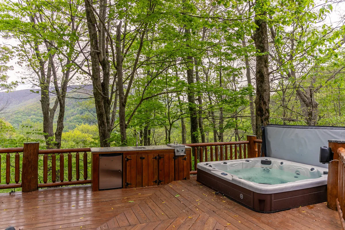 A large wooden deck with a hot tub overlooks dense trees, inviting guests to soak while surrounded by the sounds and sights of untouched nature. The scene suggests relaxation and star-gazing after a day of outdoor adventure, with the hot tub as a focal point for unwinding under the stars.