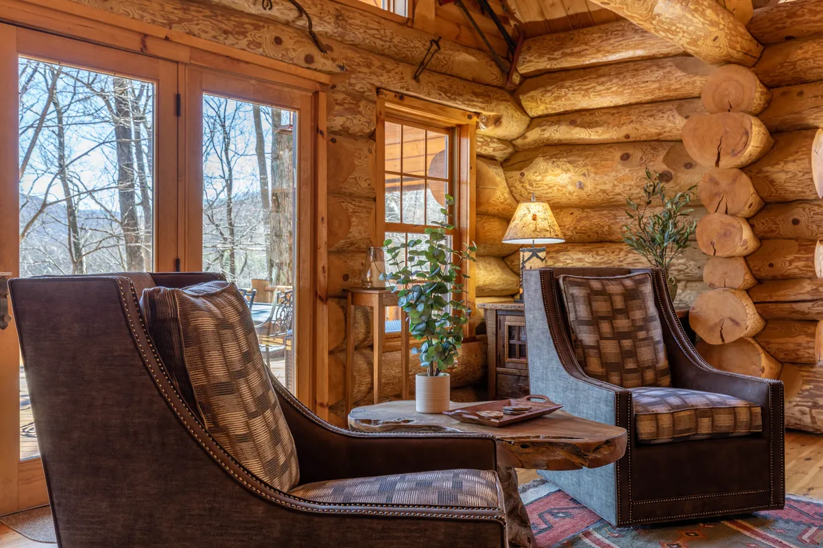 A comfortable lounge area with log walls, two armchairs, a coffee table, and windows that frame mountain views. The space exudes warmth and offers a perfect spot to unwind or watch the changing landscape outside.