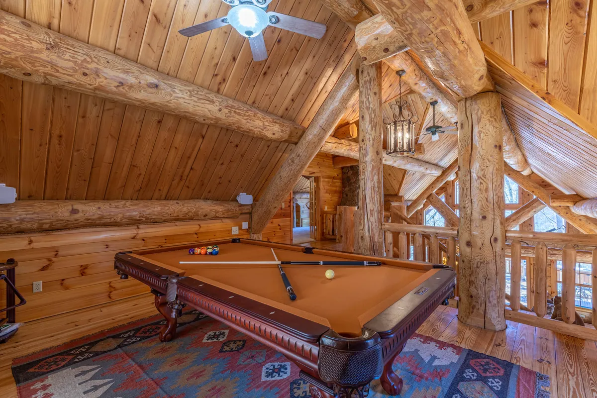 A warmly lit interior scene focusing on a pool table, surrounded by wooden beams and a cozy rug. The ambiance is friendly and relaxed, encouraging social gatherings and friendly competition.