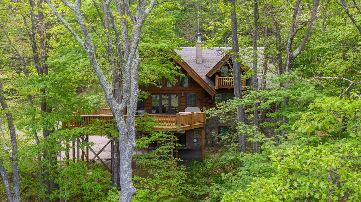 A view of the lodge’s wooden deck with large windows overlooking a forested area. The deck appears inviting and tranquil, set amidst the trees, and is ideal for relaxing after outdoor activities. The natural backdrop reinforces access to fresh mountain air and scenic views.
