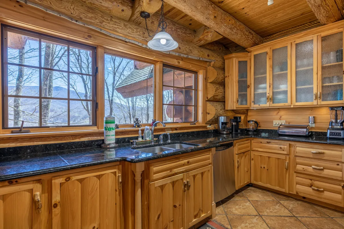A warm, inviting kitchen highlighted by large windows, wooden cabinetry, granite countertops, and modern appliances. The space is ideal for group meal preparation and socializing, offering a view into the culinary hub of the lodge.